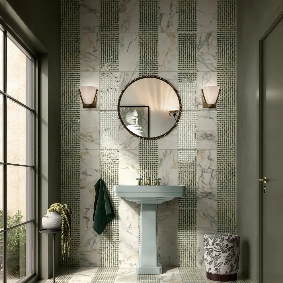 Green and white marble-effect tiles with decorative mosaic stripes in a bathroom with a mint green pedestal basin and round mirror.