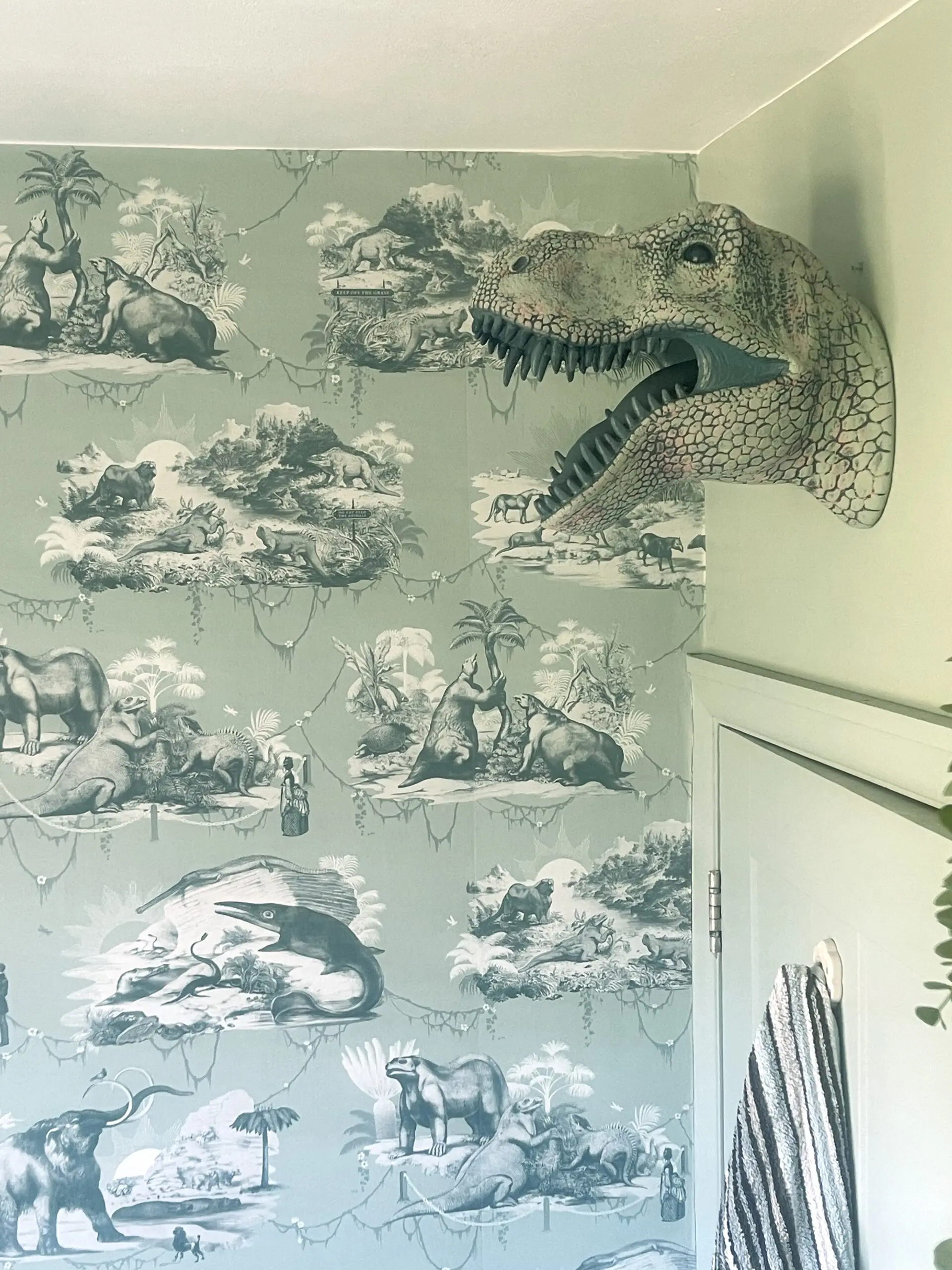 Dinosaur head over bathroom door with Divine Savages wallpaper behind
