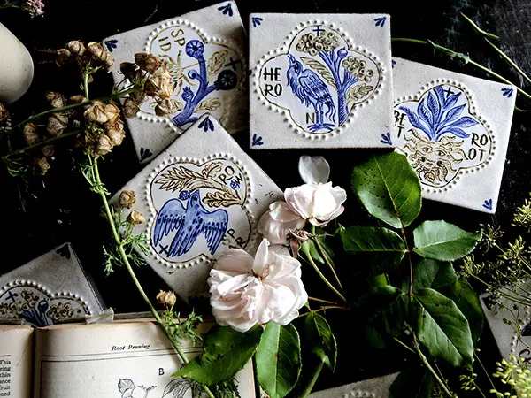 Blue and cream illustrated ceramic tiles styled with pale pink roses, foliage and an open botanical book