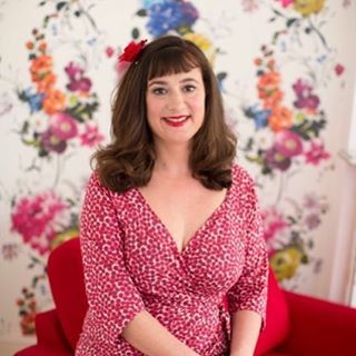 The top UK interior stylists you should be following. Picture of a brunette woman wearing a pink dress in front of a floral background