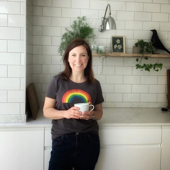 The top UK interior stylists you should be following. Lady standing in her kitchen smiling and wearing a rainbow t-shirt