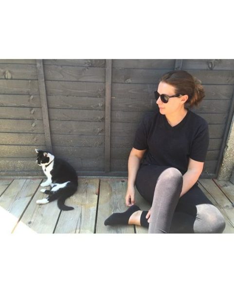 The top UK interior stylists you should be following. Woman sitting on her garden decking on a sunny day with her cat.