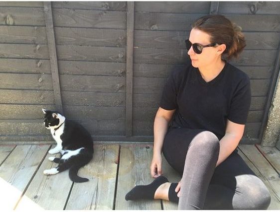The top UK interior stylists you should be following. Woman sitting on her garden decking on a sunny day with her cat.