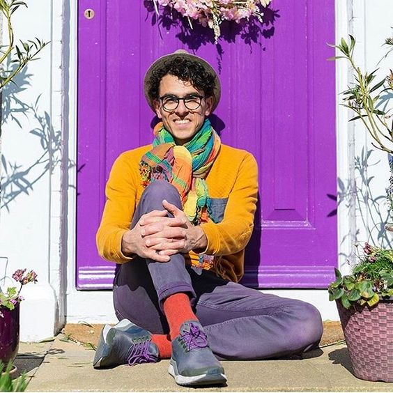 The top UK interior stylists you should be following. Man wearing brightly coloured clothes sitting in front of a purple door.