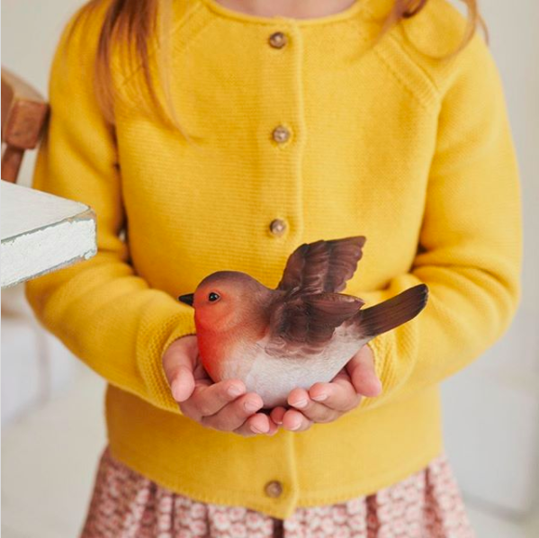 Picture of a child wearing a yellow cardigan holding a toy robin in her hands.