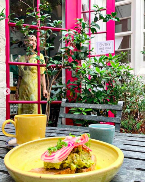 Colourful picture of a woman wearing a yellow dress standing behind a pink door 