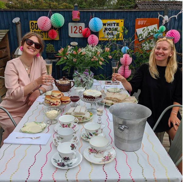 My happy place. Shot of two ladies raising a glass at an outdoor party styled with colourful pom poms and a table of afternoon tea.