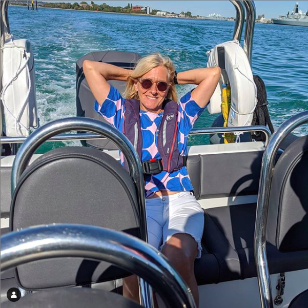 Photograph of a woman wearing sunglasses sitting on a speed boat in the summer sunshine.