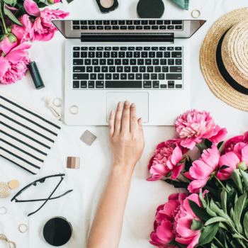 Lifestyle flat lay of a Mac laptop computer, glasses and some pink flowers