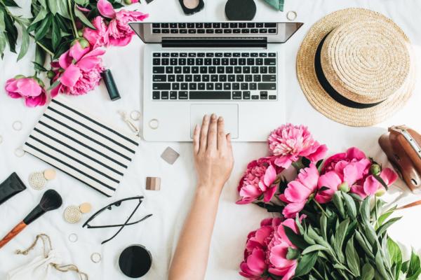 Lifestyle flat lay of a Mac laptop computer, glasses and some pink flowers