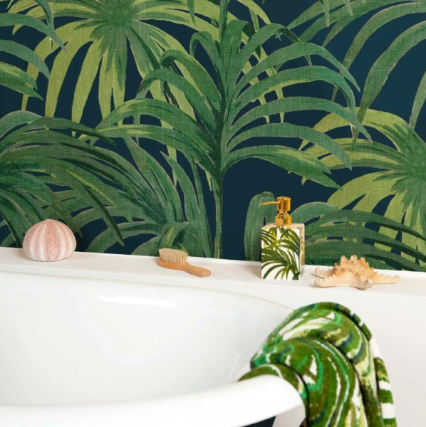 Roll top white bath in front of a bold palm tree leaf wallpaper by House of Hackney