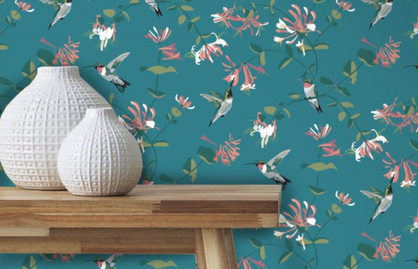 Teal wallpaper featuring hummingbirds styled behind a wooden console table and round textured vases.