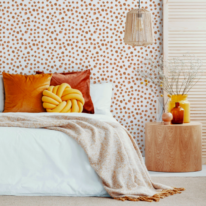 Shot of a bedroom styled with spotty terracotta wallpaper, a double bed with white linen and earth toned pillows and accessories.