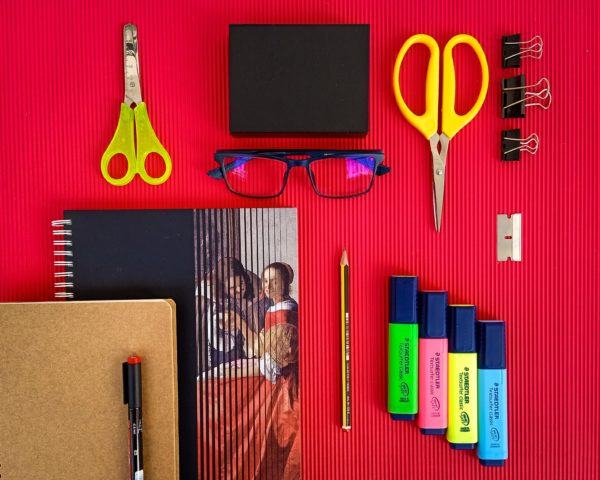 Flatlay of scissors, highlighter pens, glasses and a notebook