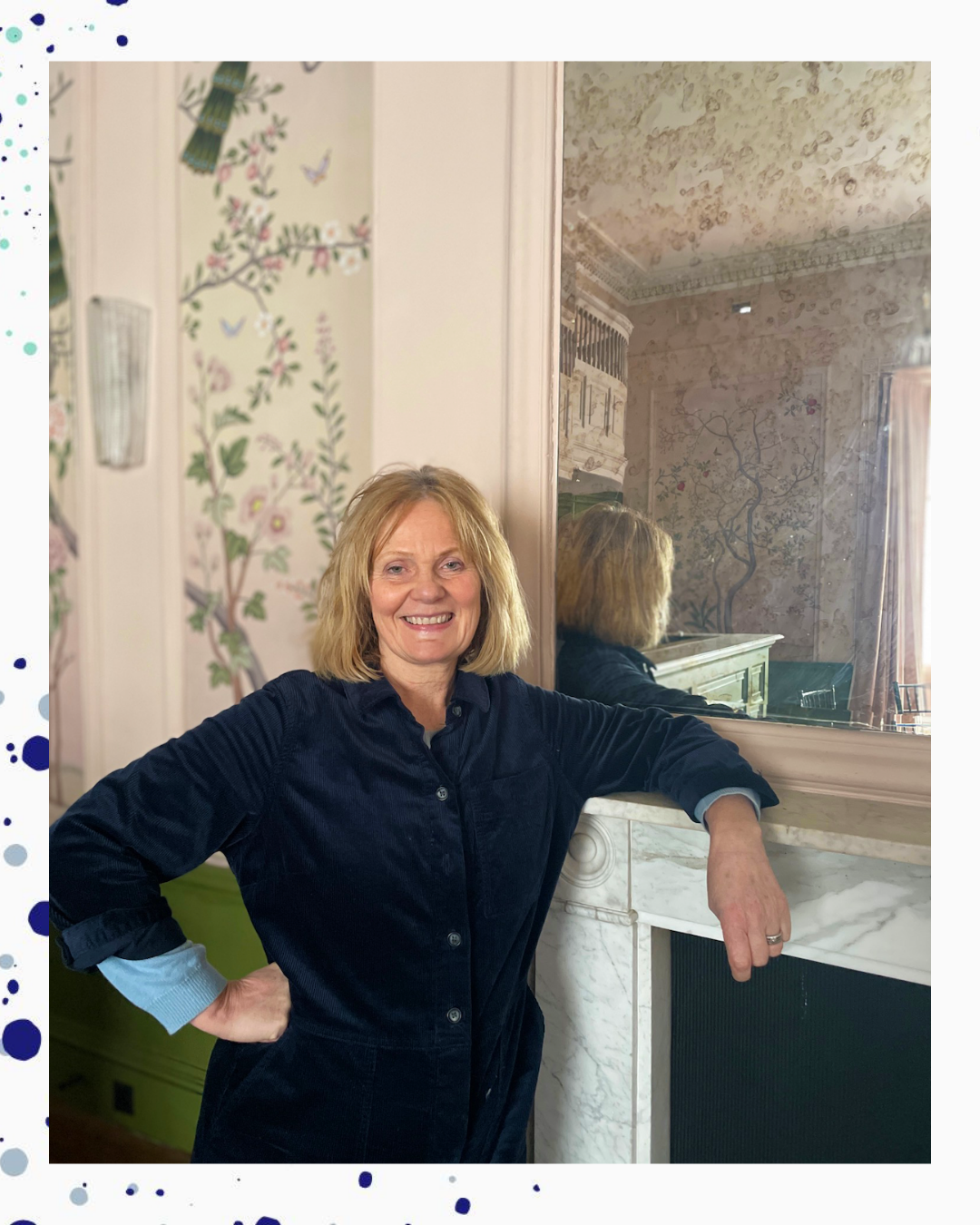 Jane Berry Interior Stylist standing in a beautiful room with floral wallpaper and a big mirror. she has a fabulous big smile 