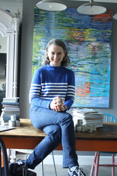 Emma Morton-Turner Sitting on her kitchen table in front of a large painting